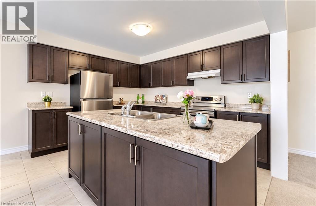 Kitchen featuring dark wood-finish cabinetry, light-toned countertops, stainless steel appliances, a center island with an integrated sink, and tile flooring - 61 Duckworth Road, Cambridge, ON