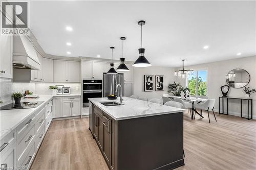Open-concept living space with wood-finish flooring, a kitchen island with integrated sink, white shaker-style cabinetry, and stainless steel appliances - 46 Esther Avenue, Cambridge, ON 
