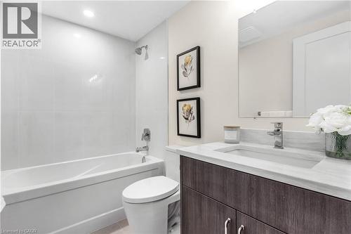 Full-size bathtub with subway tile surround, vanity with an integrated sink, chrome faucet, and wood-finish cabinetry - 46 Esther Avenue, Cambridge, ON 