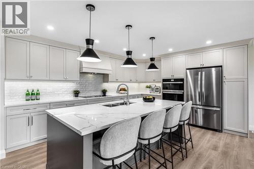 Kitchen featuring an expansive island with a waterfall countertop, light-toned cabinetry, stainless steel appliances, and wood-finish flooring - 46 Esther Avenue, Cambridge, ON 