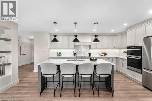 Kitchen featuring a large central island, light-finish cabinetry, built-in double ovens, stainless steel refrigerator, and wood-finish flooring - 46 Esther Avenue, Cambridge, ON 
