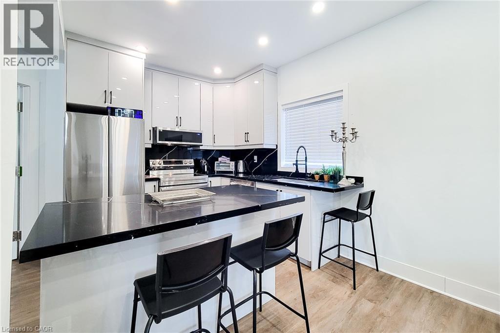 Sleek kitchen featuring white cabinetry, black countertops, stainless steel appliances, and wood-finish flooring - 78 Hillyard Street, Hamilton, ON