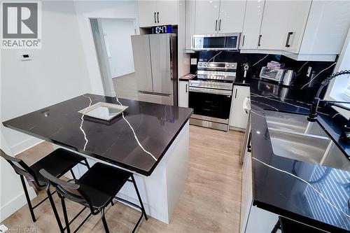 Kitchen featuring wood-finish flooring, white cabinetry with dark hardware, a double basin sink with a gooseneck faucet, black countertops with white veining, and stainless steel appliances - 78 Hillyard Street, Hamilton, ON 