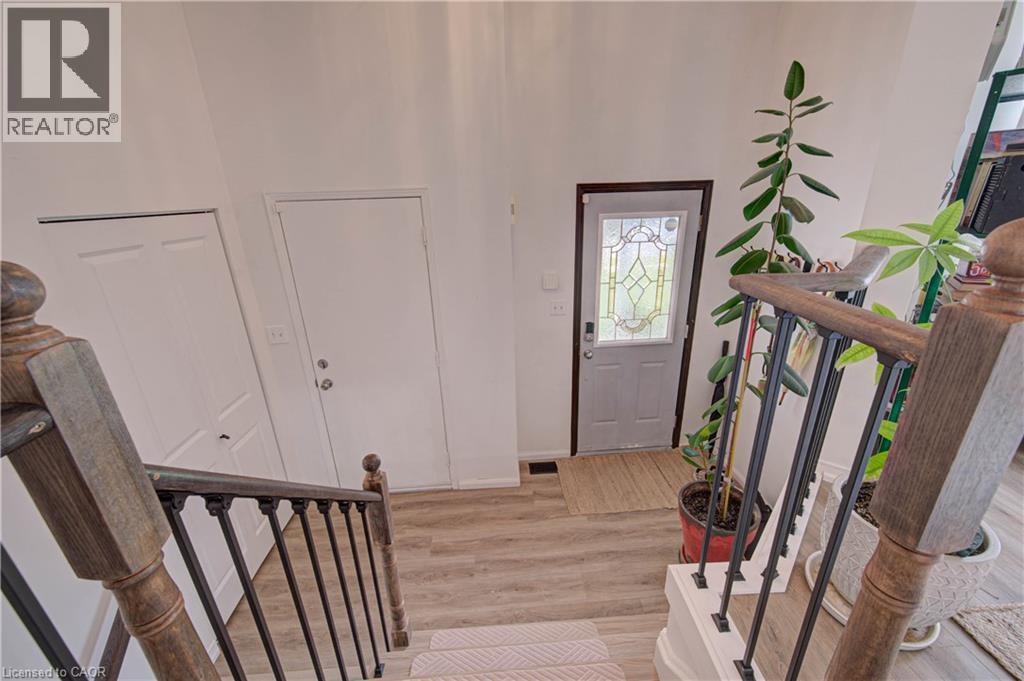 Wood-finish flooring, staircase with wood banister, wrought iron balusters, and decorative glass panel door - 317 Christopher Drive, Cambridge, ON