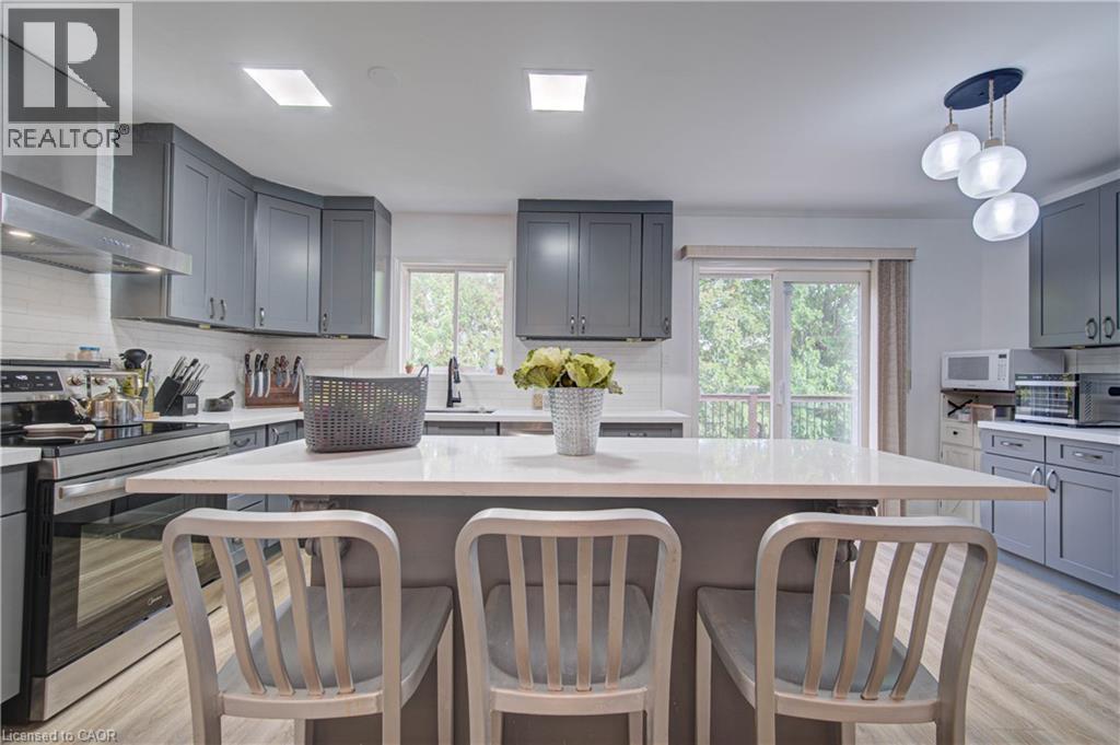 Kitchen featuring gray cabinetry, stainless steel appliances, an integrated kitchen island, light wood-finish flooring, and a sliding glass door - 317 Christopher Drive, Cambridge, ON