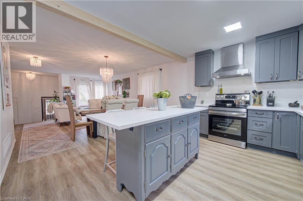 Kitchen featuring a central island with white countertop, grey cabinetry, stainless steel appliances, and wood-finish flooring - 317 Christopher Drive, Cambridge, ON