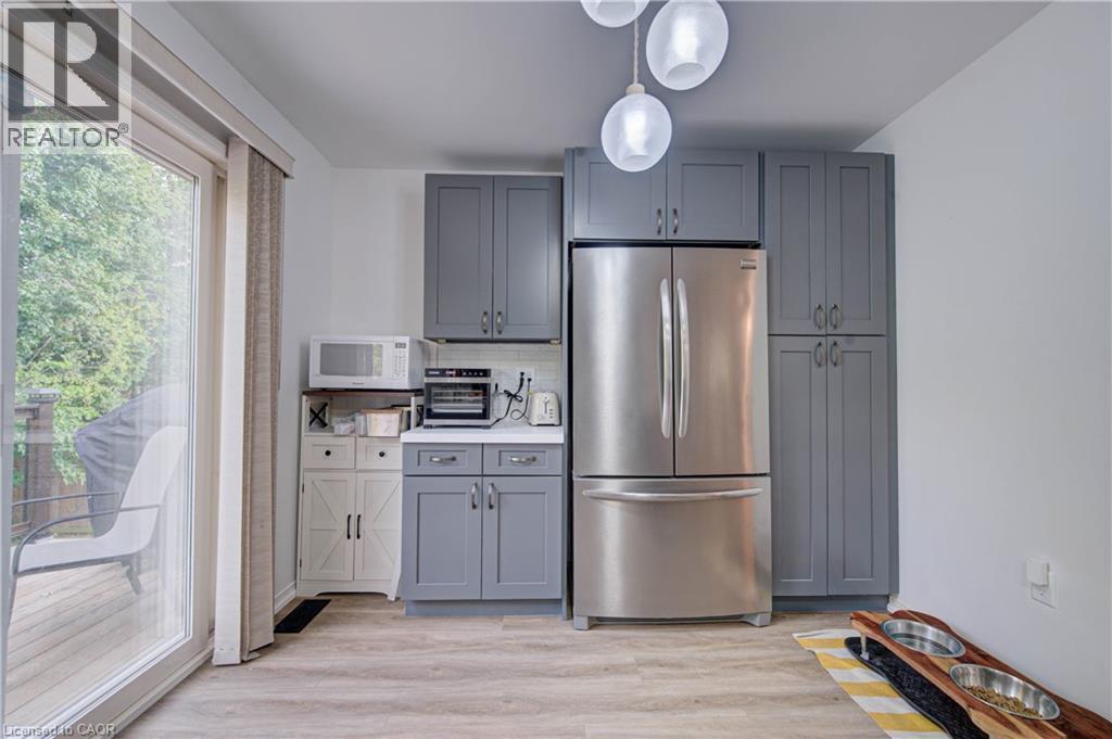 Gray shaker-style cabinetry, stainless steel refrigerator, white countertops, wood-finish flooring, and sliding glass door - 317 Christopher Drive, Cambridge, ON