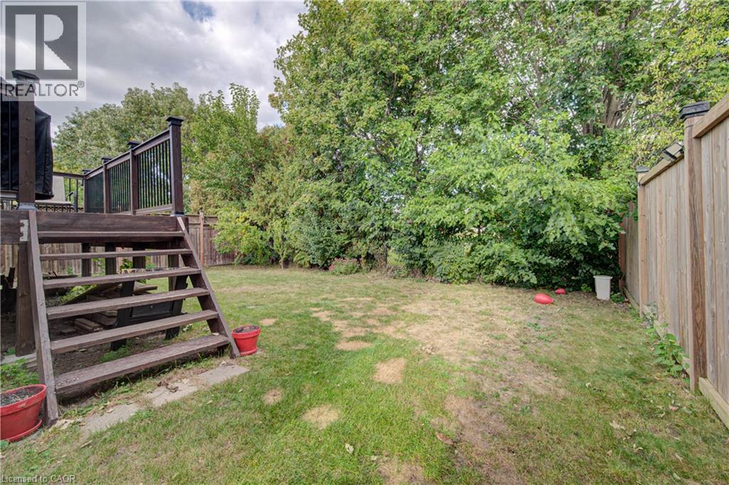 Expansive grassy yard area with a multi-level deck, dark wood stairs, and a tall wood privacy fence - 317 Christopher Drive, Cambridge, ON