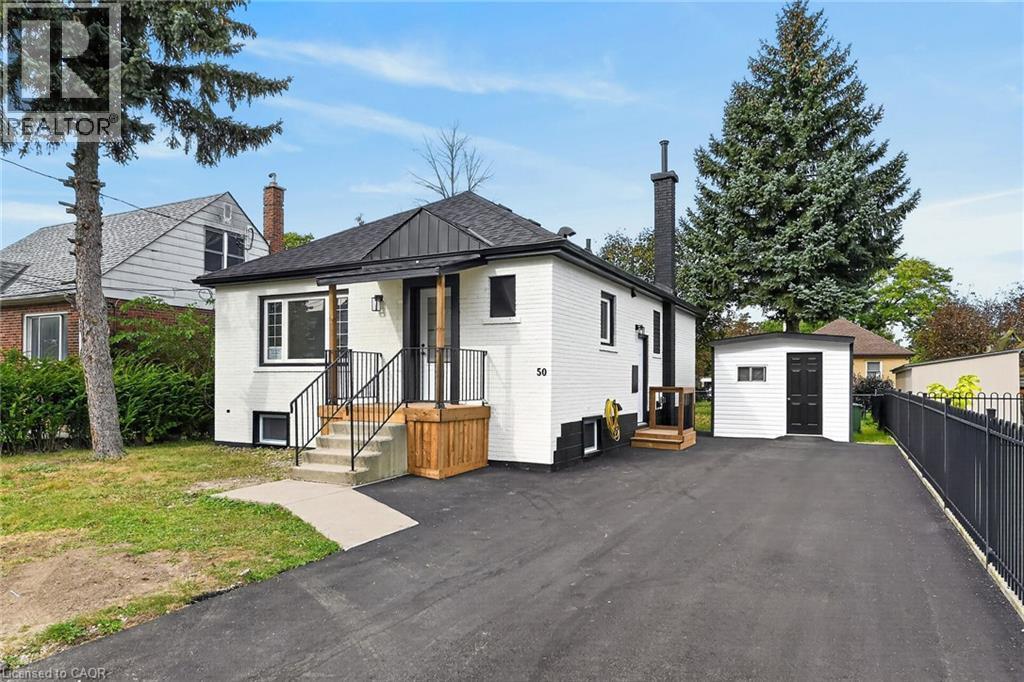White brick exterior with black trim, black shingle roof, paved driveway, detached storage shed, and a black metal fence - 50 West 4Th Street, Hamilton, ON