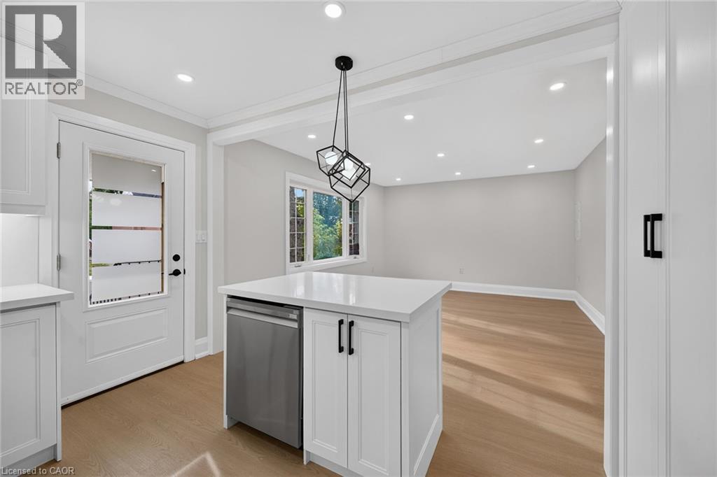 Kitchen island with quartz countertop and integrated stainless steel dishwasher, illuminated by a geometric pendant light - 50 West 4Th Street, Hamilton, ON
