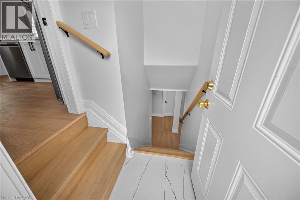 Wood-finish flooring, white paneled door with brass hardware, and a wooden handrail - 50 West 4Th Street, Hamilton, ON