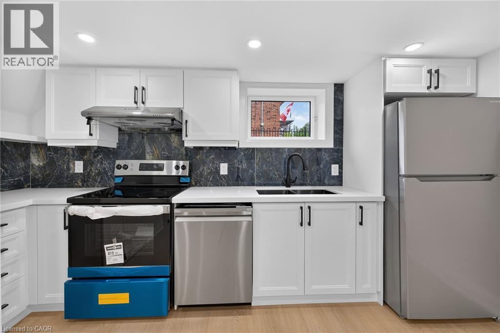 White shaker-style cabinetry with matte black hardware, stainless steel appliances, dark stone-finish backsplash, white countertops, and wood-finish flooring - 50 West 4Th Street, Hamilton, ON
