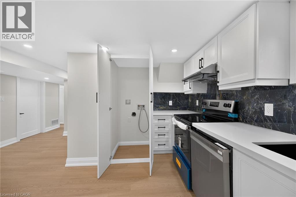 White shaker cabinetry, black marble-patterned backsplash, white countertops, built-in range, and wood-finish flooring - 50 West 4Th Street, Hamilton, ON