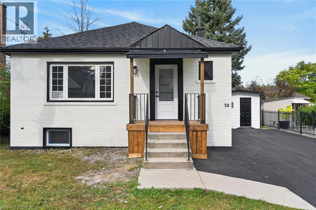 White brick exterior with black trim, covered porch with natural wood accents, concrete steps, and paved driveway - 50 West 4Th Street, Hamilton, ON