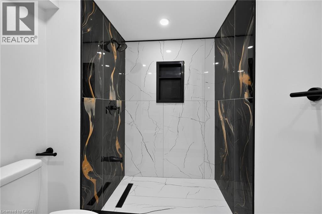 Tiled shower stall with black and white veined tile, contrasting black and gold accent tiles, matte black shower fixtures, and a recessed shower niche - 50 West 4Th Street, Hamilton, ON