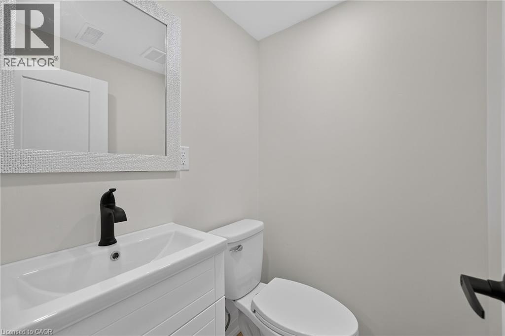 White vanity with a rectangular basin sink, matte black faucet, and a textured framed mirror - 50 West 4Th Street, Hamilton, ON