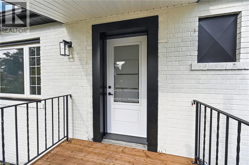 White painted brick exterior with black trim, a wood-finish porch, and black metal railings - 50 West 4Th Street, Hamilton, ON