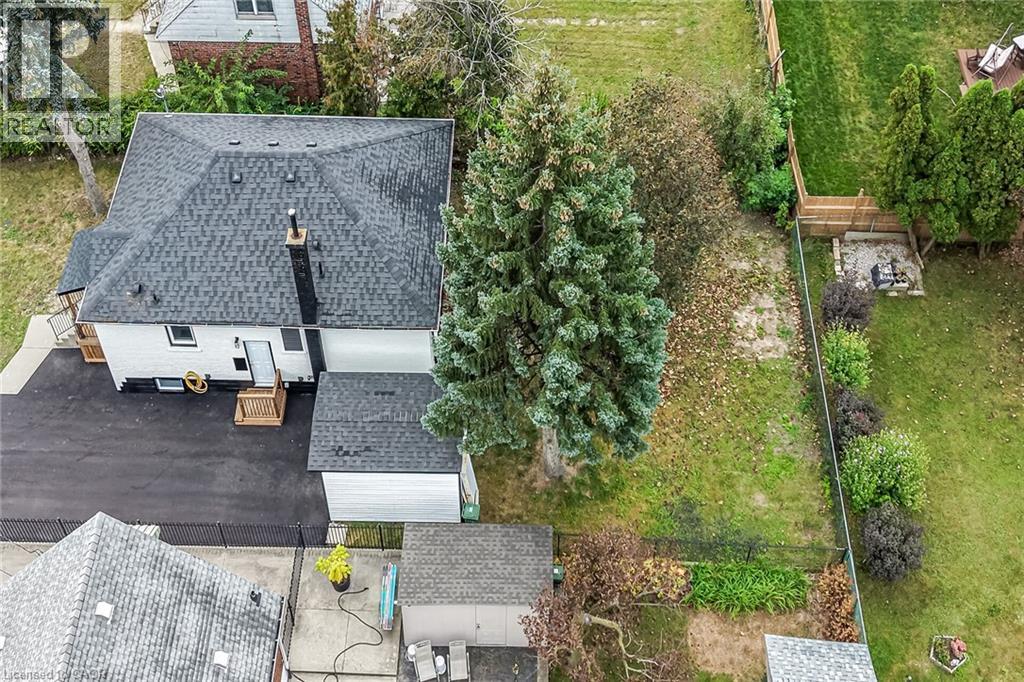Expansive backyard featuring a manicured lawn, established landscaping, privacy fencing, and a fire pit area - 50 West 4Th Street, Hamilton, ON