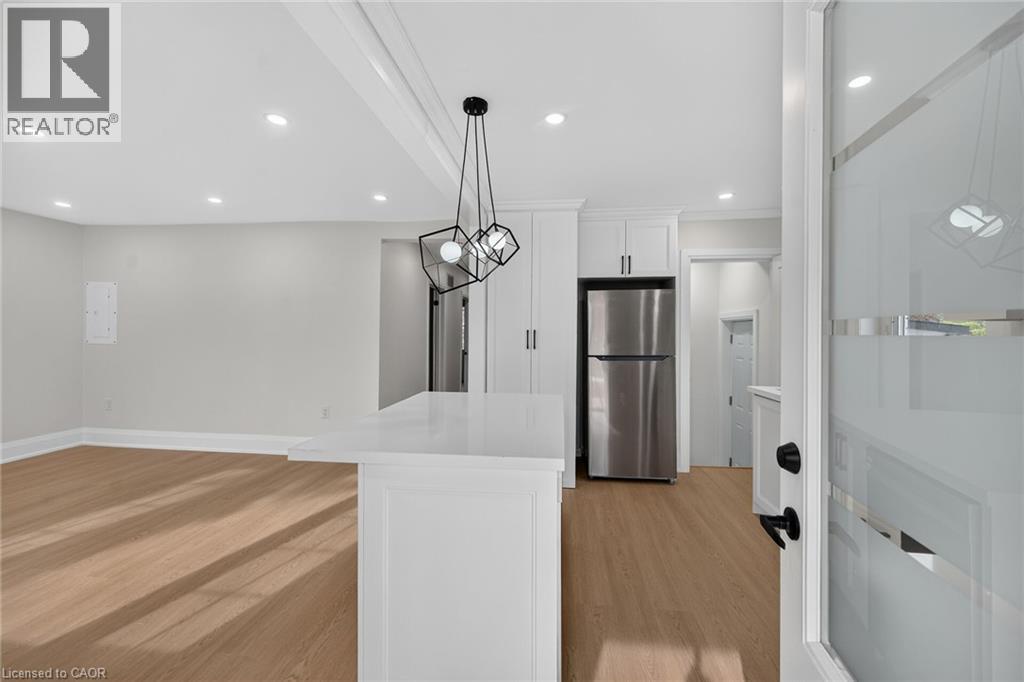 Wood-finish flooring, recessed ceiling lighting, kitchen island with a white countertop, modern geometric pendant lighting, and stainless steel refrigerator - 50 West 4Th Street, Hamilton, ON