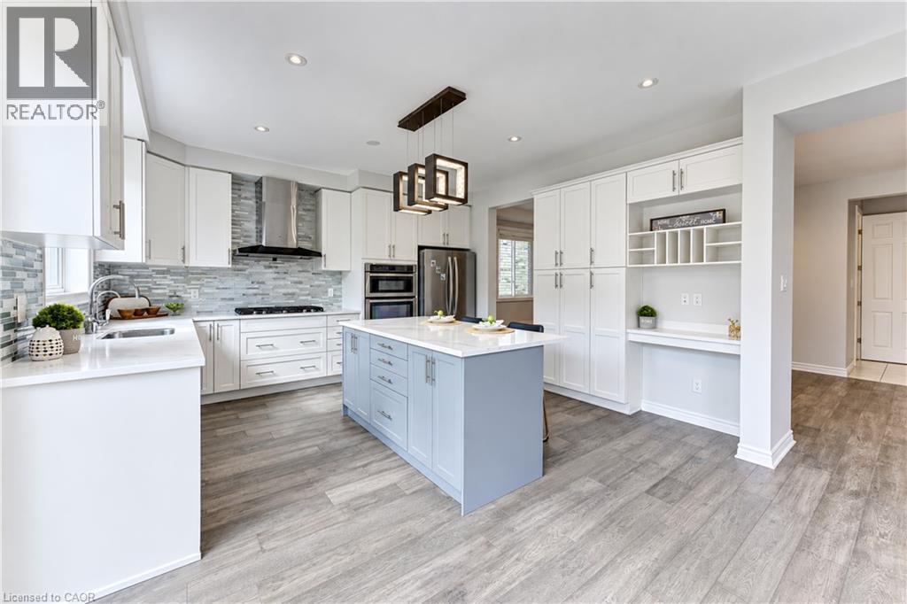 Contemporary kitchen featuring white cabinetry, a blue central island with a solid surface countertop, stainless steel appliances, a tile backsplash, and wood-finish flooring - 365 Woolwich Street, Waterloo, ON