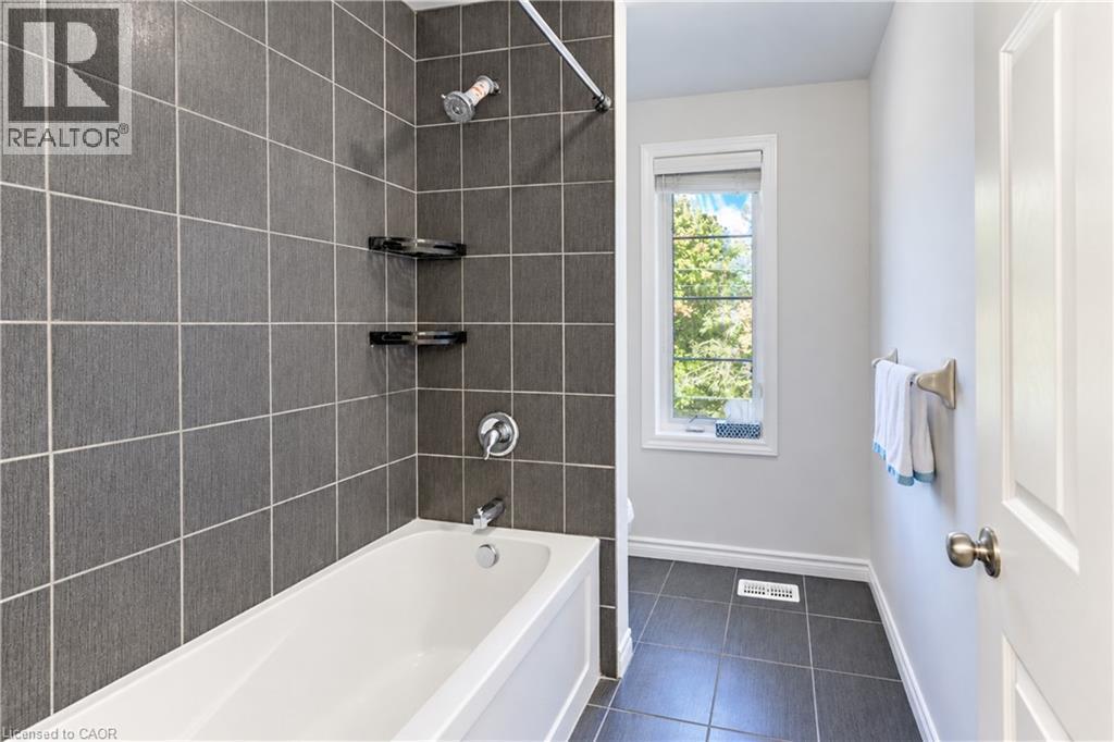 White bathtub with chrome fixtures, dark gray tile surround, and built-in shelving - 365 Woolwich Street, Waterloo, ON