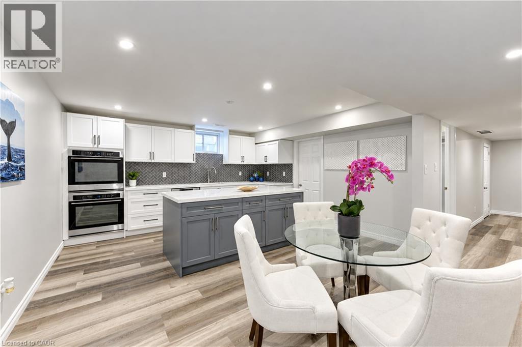 Kitchen featuring recessed lighting, wood-finish flooring, two-tone cabinetry, stainless steel built-in ovens, and a kitchen island with a light-colored countertop - 365 Woolwich Street, Waterloo, ON
