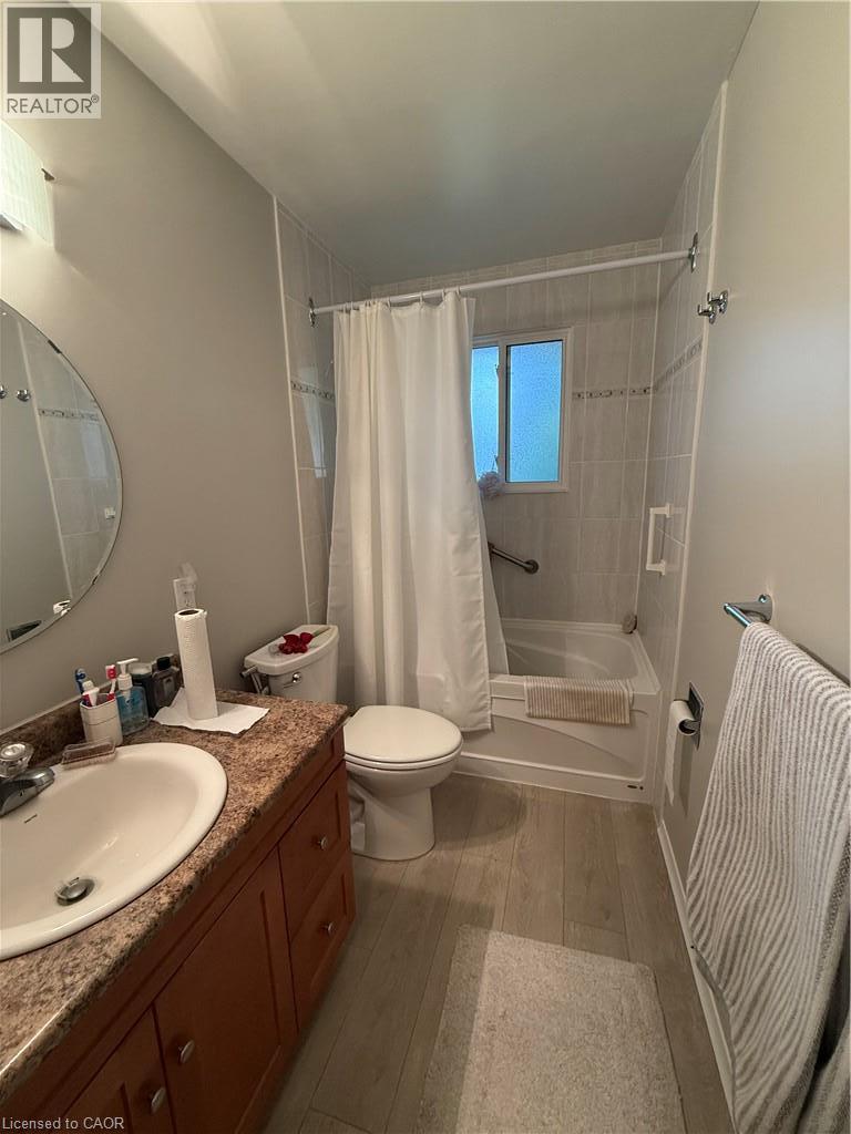 Bathroom featuring a vanity with an integrated sink, wood-finish cabinetry, a tub-shower combination with tiled surround, and wood-finish flooring - 281 Toll Gate Boulevard, Waterloo, ON