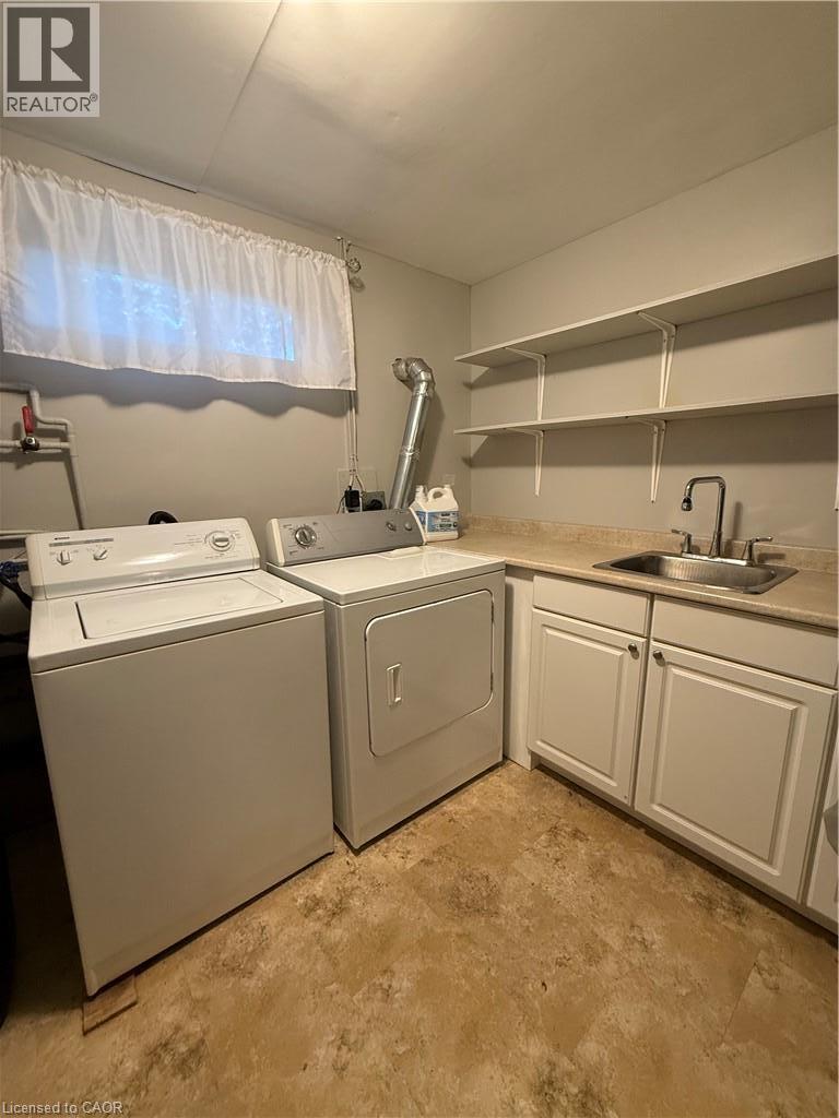 Laundry area featuring light-toned walls, a window with white curtains, a utility sink with a faucet, white cabinetry, and white open shelving - 281 Toll Gate Boulevard, Waterloo, ON
