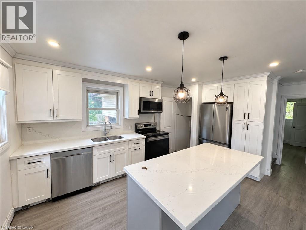 Kitchen featuring white shaker cabinetry, stainless steel appliances, a center island with a stone-finish countertop, and wood-finish flooring - 84 Weber Street S, Waterloo, ON