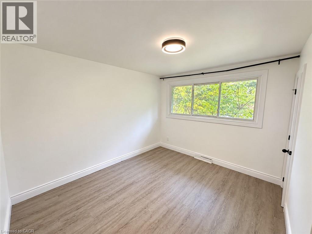 Wood-finish flooring with white baseboards, a flush-mount ceiling light, a multi-pane window, and a white door with dark hardware - 84 Weber Street S, Waterloo, ON