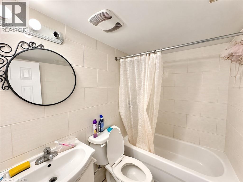 White tiled shower surround with a built-in tub, white porcelain sink, and wall-mounted vanity lighting - 84 Weber Street S, Waterloo, ON