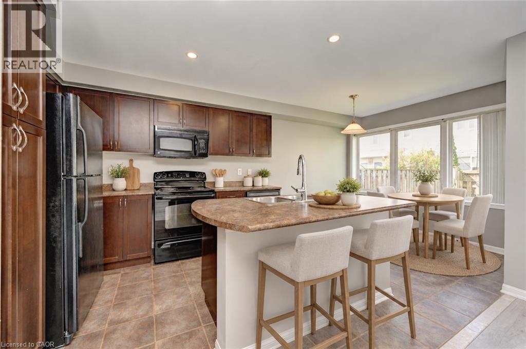 Rich wood-finish cabinetry, black appliances, a central island with an integrated sink, and an adjacent dining area with broad windows - 103 Blackbird Circle, Cambridge, ON