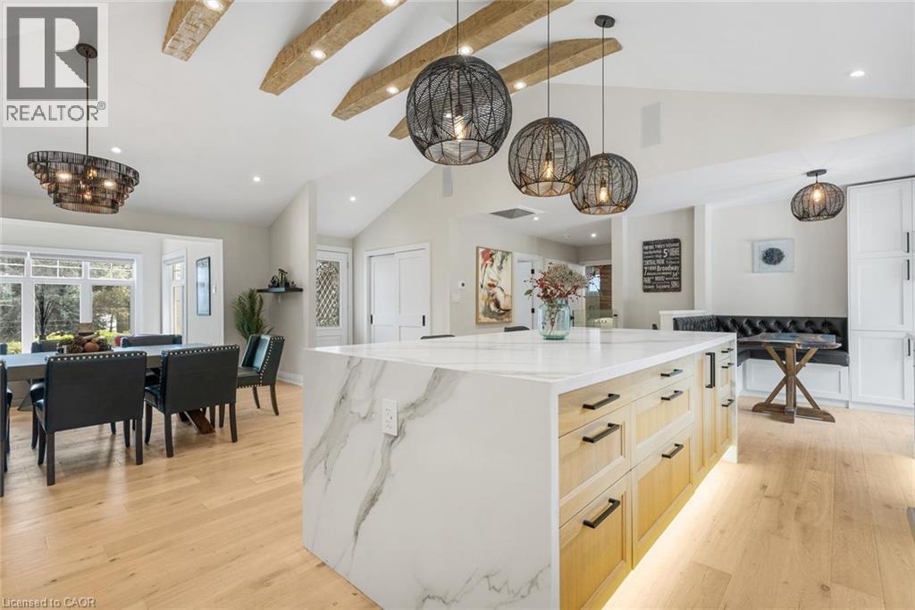 Vaulted ceilings with exposed beams, wood-finish flooring, waterfall island with a light-toned countertop, custom built-in seating, and modern pendant lighting - 293 North Shore Boulevard E, Burlington, ON