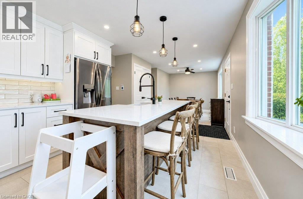 White shaker-style cabinetry with matte black hardware, stainless steel refrigerator, elongated subway tile backsplash, white countertop island with integrated sink, and recessed lighting - 37 Margaret Avenue N, Waterloo, ON