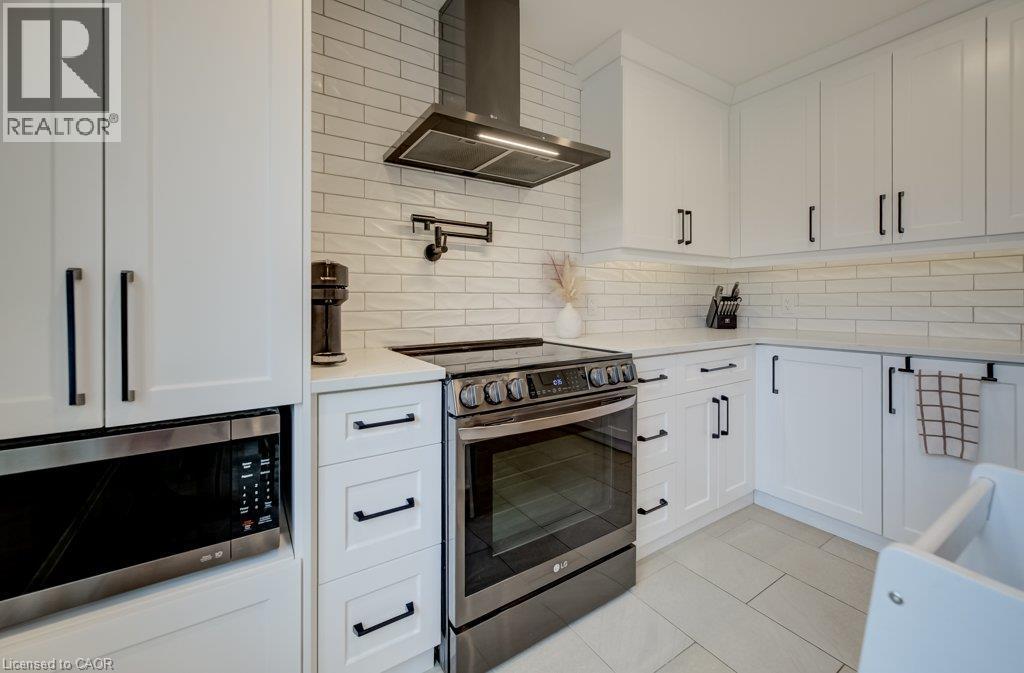 White shaker-style cabinetry with black hardware, stainless steel appliances, light-toned subway tile backsplash, white countertops, and light-toned tile flooring - 37 Margaret Avenue N, Waterloo, ON