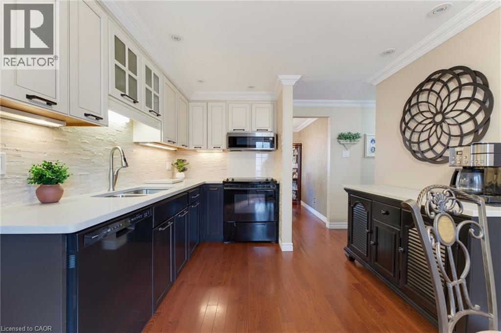 Kitchen featuring white upper cabinetry, dark lower cabinetry and hardwood flooring. - 77 Yellow Birch Drive, Kitchener, ON