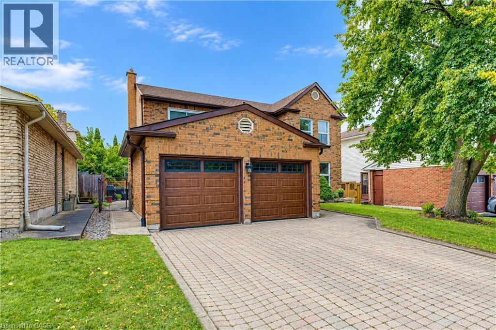 Brick exterior residence featuring a two-car garage with wood-finish doors, a paver driveway, and a manicured lawn - 104 Deerwood Crescent, Kitchener, ON