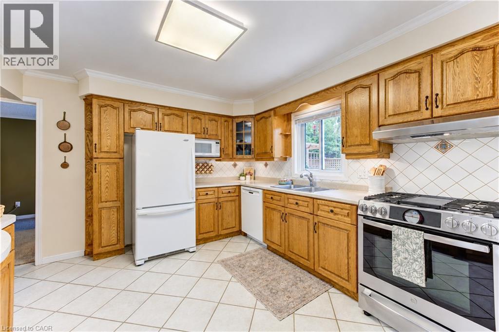Kitchen featuring wood cabinetry, white tile flooring, stainless steel range, white appliances, and a window above the sink - 104 Deerwood Crescent, Kitchener, ON