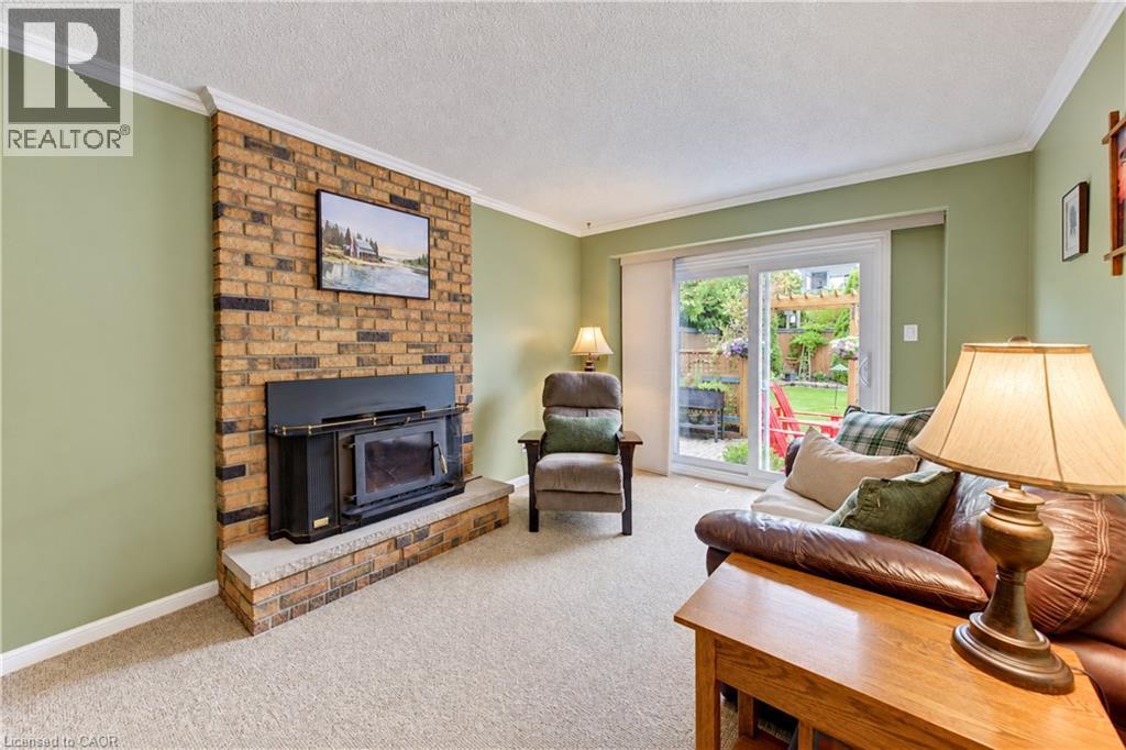 Brick-clad fireplace with a wood-burning insert, crown molding, and sliding glass doors leading to the outdoor space - 104 Deerwood Crescent, Kitchener, ON