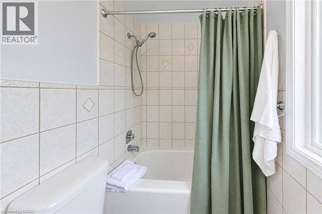 Bathtub and shower combination featuring a flexible showerhead, tiled surround with decorative accents, and a window providing natural light - 104 Deerwood Crescent, Kitchener, ON