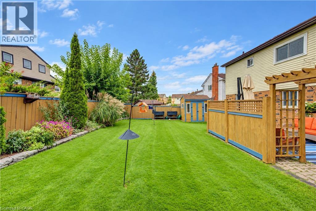 Expansive lawn with perimeter landscaping, wood fencing, and a detached shed - 104 Deerwood Crescent, Kitchener, ON