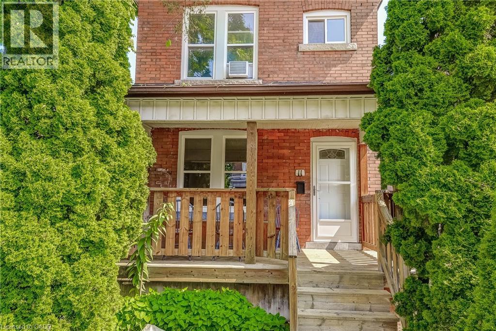 Brick exterior with a covered porch, wood-finish railing, and mature evergreen plantings - 11 Elm Street, Hamilton, ON