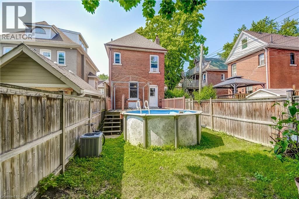 Fenced backyard with an above-ground pool, brick exterior, and wood deck - 11 Elm Street, Hamilton, ON