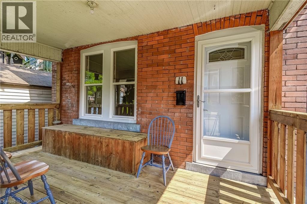 Covered wood-plank porch with brick wall siding, wood railing, and white-framed windows - 11 Elm Street, Hamilton, ON