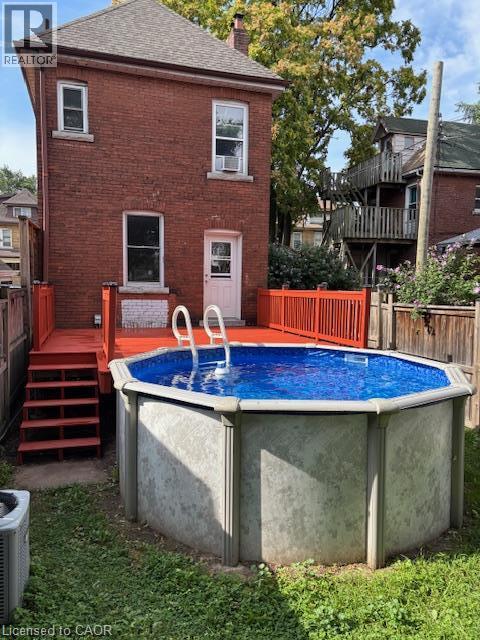 Red brick exterior featuring an above-ground pool, a red-painted deck, and exterior stairs - 11 Elm Street, Hamilton, ON