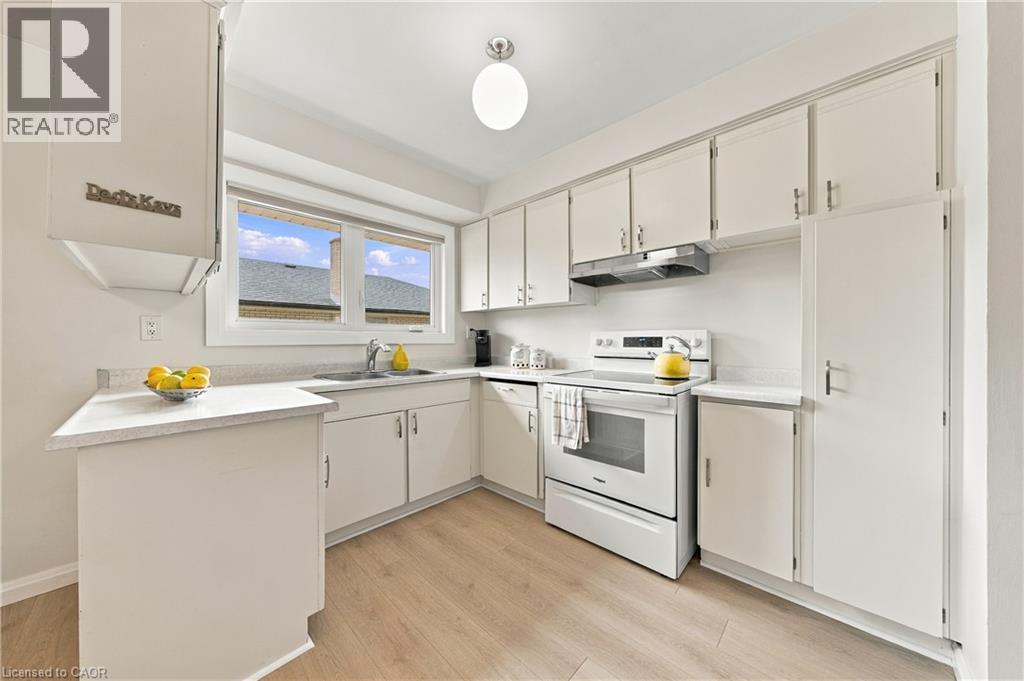 Kitchen featuring white cabinetry, wood-finish flooring, white appliances, and a window above the sink - 662 Dynes Road, Burlington, ON