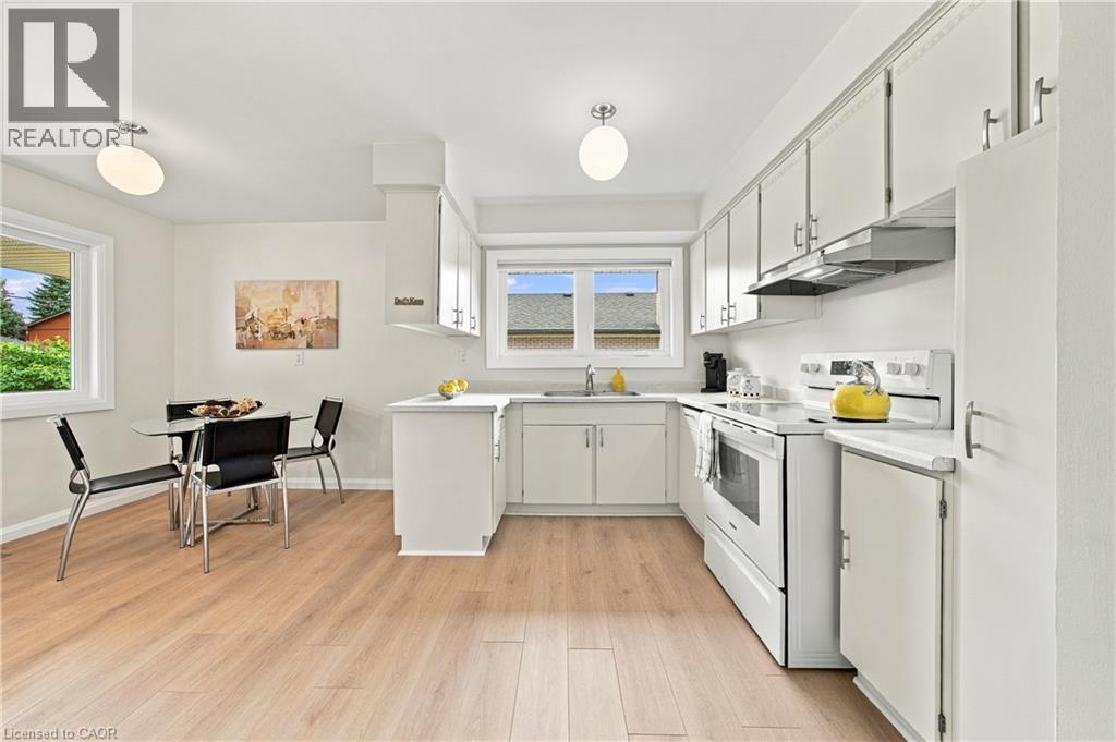 White cabinetry with brushed nickel hardware, light wood-finish flooring, white appliances, and a window above the sink - 662 Dynes Road, Burlington, ON