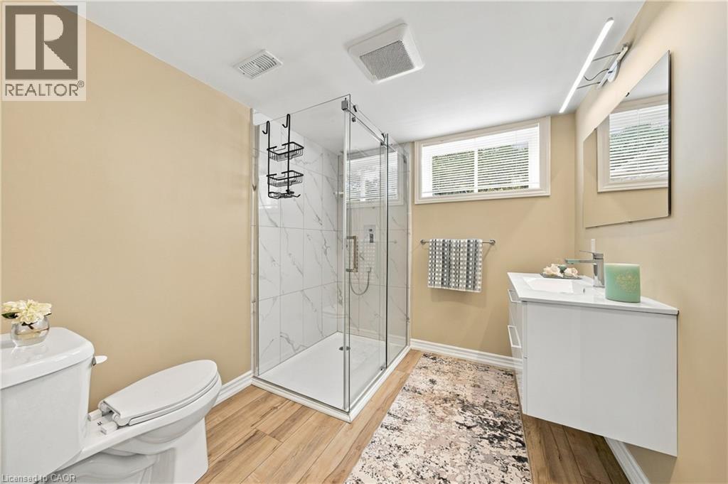 Glass-enclosed shower with white marble-look tile, wood-finish flooring, a white floating vanity with a vessel sink, and a rectangular mirror - 662 Dynes Road, Burlington, ON