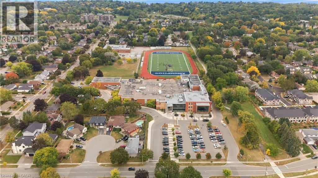Aerial perspective of a developed neighborhood featuring residential properties, mature trees, and a school building with an athletic field - 662 Dynes Road, Burlington, ON