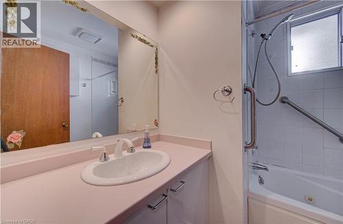 Bathroom featuring a vanity with an integrated sink, a large wall-mounted mirror, a bathtub with a shower attachment, and an obscured window - 465 Herkimer Street, Hamilton, ON 